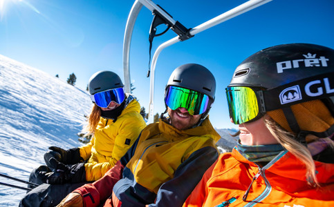 Drei Wintersportler in einem Sessellift bei Sonnenschein und blauem Himmel